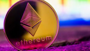 Eine goldene Ethereum Treasury-Münze steht aufrecht auf einer lilafarbenen Oberfläche mit einem unscharfen, bunten Hintergrund.