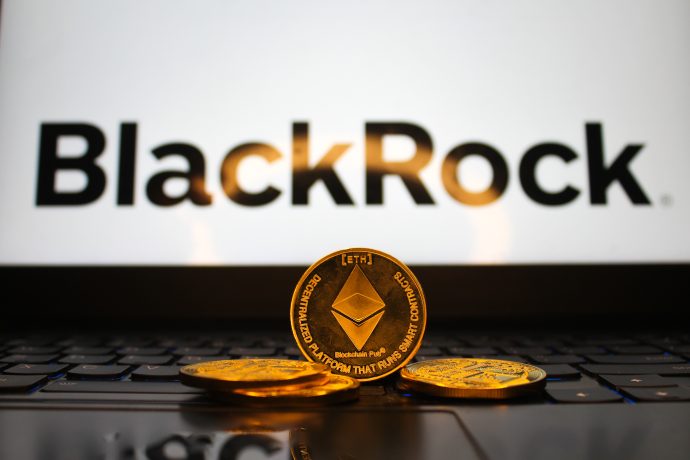 Drei Ethereum-Münzen liegen auf einer Laptop-Tastatur, während im Hintergrund das BlackRock-Logo auf dem Bildschirm angezeigt wird.