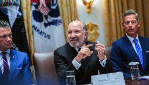 Howard Lutnick spricht an einem Konferenztisch, flankiert von zwei weiteren Anzugträgern. Auf einem Namensschild steht "Howard Lutnick, Secretary of Commerce", während er über die Auswirkungen von Chainlink auf die Zuverlässigkeit von Wirtschaftsdaten spricht.