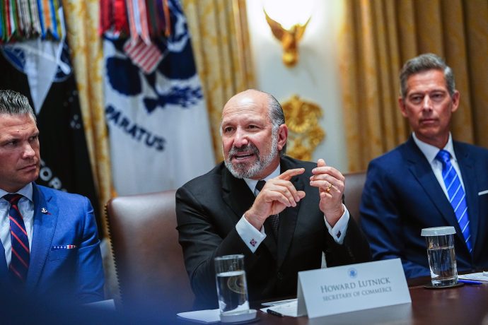 Howard Lutnick spricht an einem Konferenztisch, flankiert von zwei weiteren Anzugträgern. Auf einem Namensschild steht "Howard Lutnick, Secretary of Commerce", während er über die Auswirkungen von Chainlink auf die Zuverlässigkeit von Wirtschaftsdaten spricht.