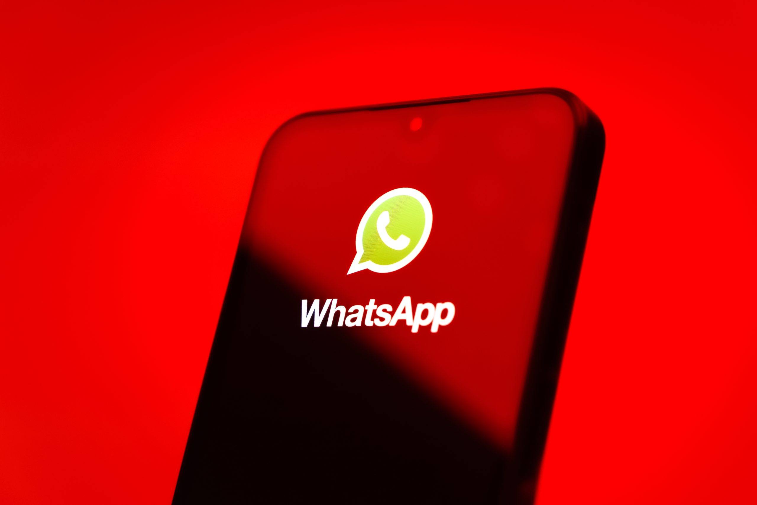 Auf einem Smartphone-Bildschirm werden das WhatsApp-Logo und der Name vor einem roten Hintergrund angezeigt - eine Anspielung auf die Besorgnis über Krypto-Betrug und die Erinnerung an Konten löschen für die Sicherheit.