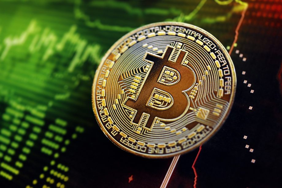 Eine physische Bitcoin-Münze wird über einem digitalen Diagramm gezeigt, das Finanzdaten mit grünen und roten Linien anzeigt.