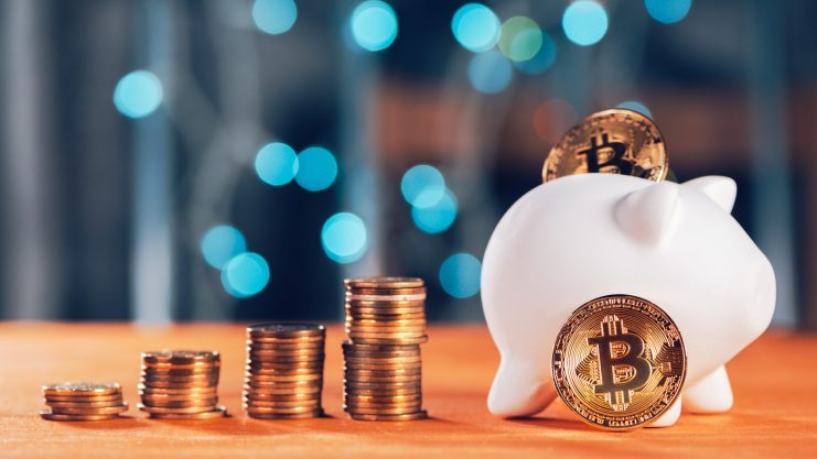Ein weißes Sparschwein mit Bitcoin-Token und vier Stapeln von Münzen auf einer hölzernen Oberfläche, die Bitcoin in Rente symbolisiert, mit blauen Lichtern im Hintergrund verschwommen. Das soll das Sparen in Bitcoin symbolisieren, womit man frühzeitig in Rente gehen kann.