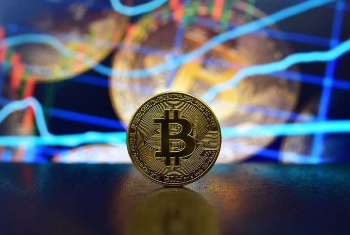 Eine goldene Bitcoin-Münze steht aufrecht auf einem Tisch, während digitale Charts und Finanzdiagramme die Bitcoin-Trends im verschwommenen Hintergrund hervorheben.
