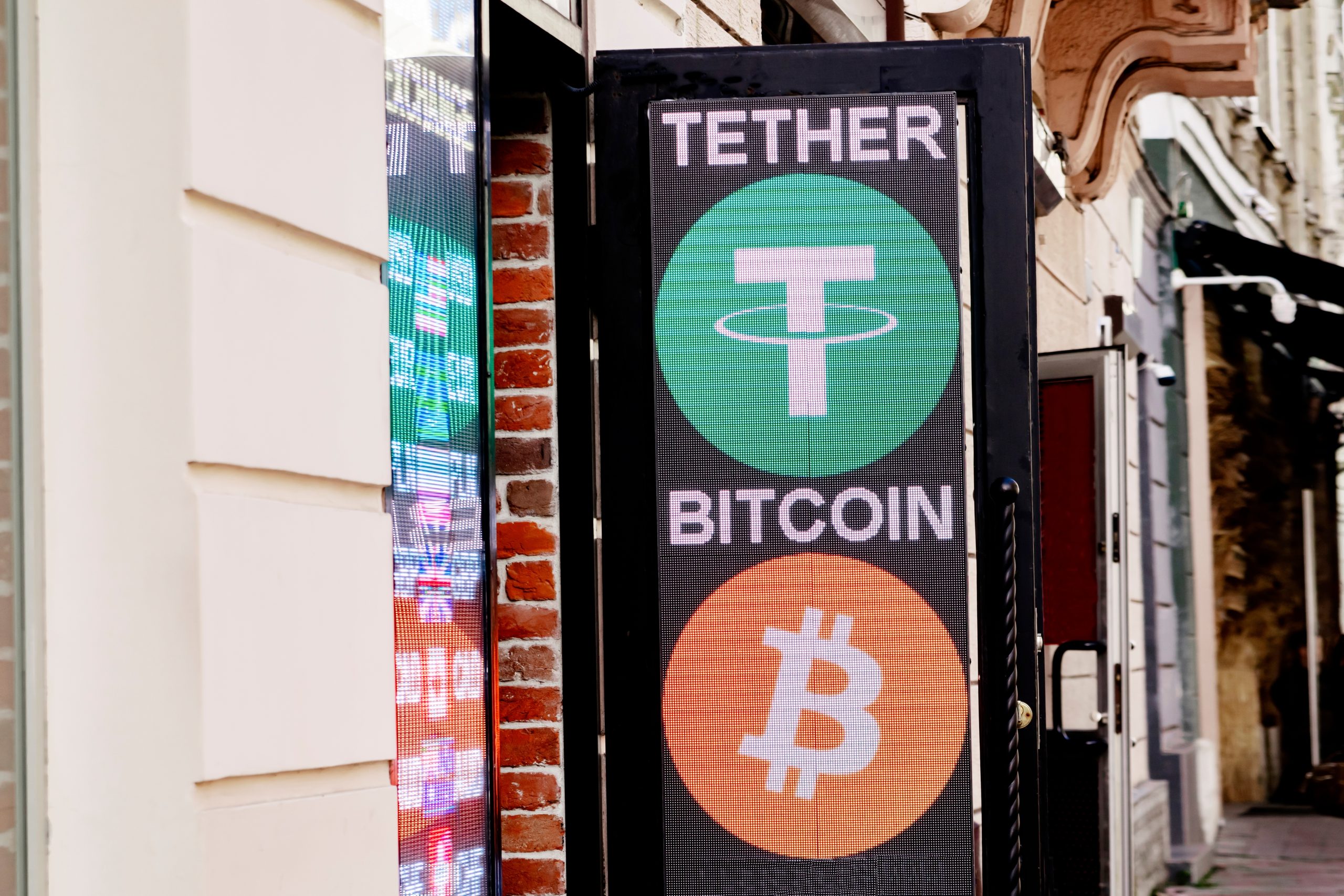 Ein Schild vor einem Gebäude zeigt die Logos und Namen beliebter Kryptowährungen, darunter Tether und Bitcoin.