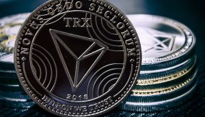 Eine Nahaufnahme einer Tron (TRX) Kryptowährungsmünze steht aufrecht vor gestapelten Münzen und zeigt detaillierte Gravuren und den Text NOVUS ORDO SECLORUM und IN TRON WE TRUST.