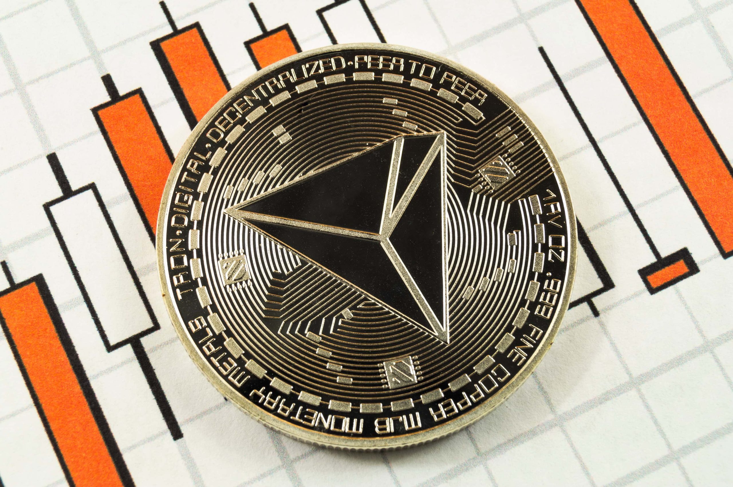 Eine Tron (TRX) Kryptowährungsmünze auf einem Kerzenchart mit orangen und schwarzen Linien.