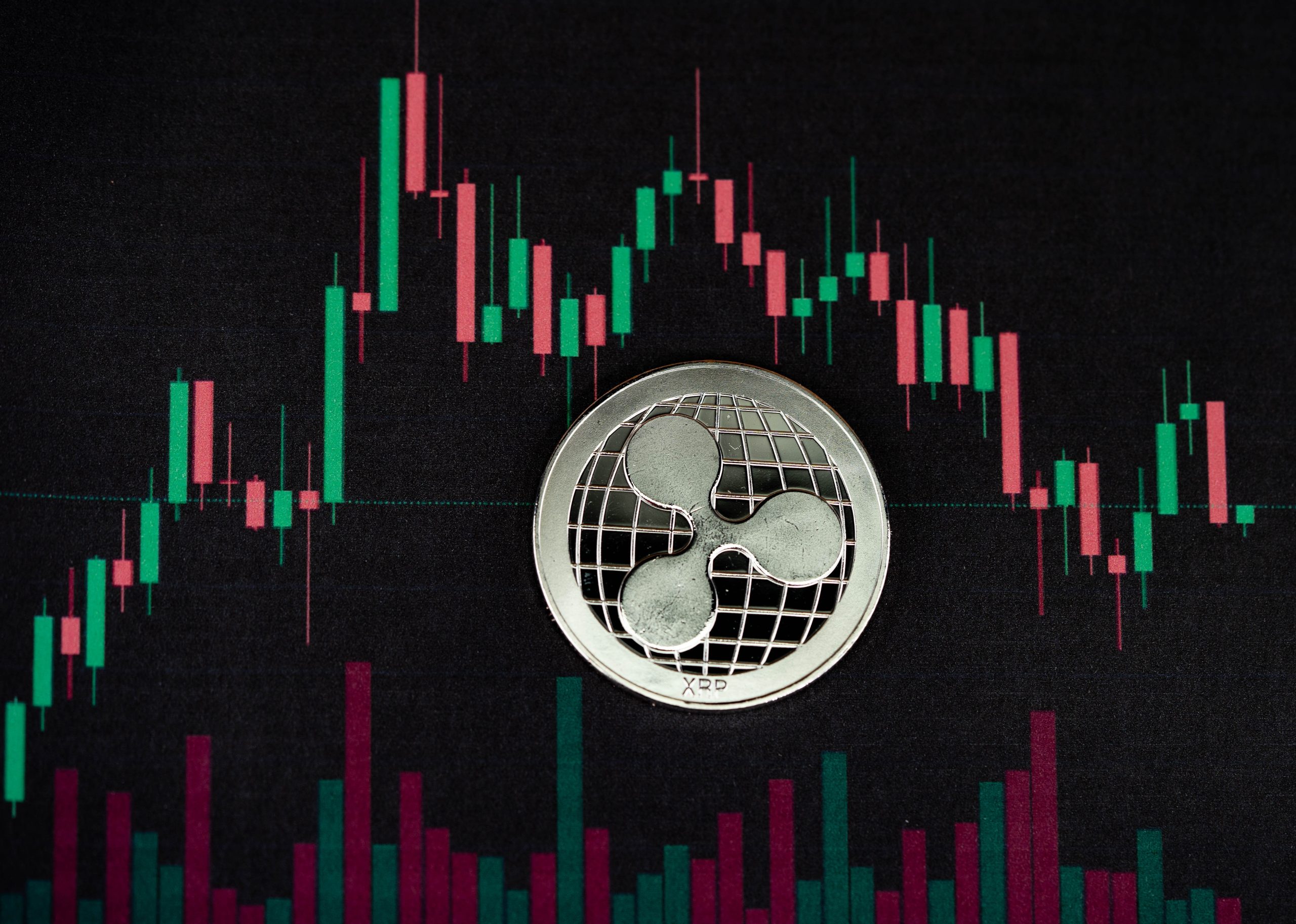 Eine Ripple-Münze (XRP) auf einem digitalen Bildschirm, der ein Candlestick-Diagramm mit roten und grünen Balken anzeigt, das die Handelsdaten von Kryptowährungen und das wachsende Interesse an Spot-ETFs darstellt.