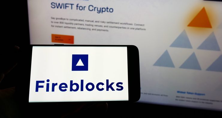 Ein Smartphone-Bildschirm zeigt das Fireblocks-Logo vor einem Monitor, der die SWIFT for Crypto-Seite auf der Fireblocks-Website zeigt und die Integration mit Euro-Stablecoin-Lösungen hervorhebt.