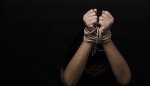 Eine Person, deren Hände mit einem Seil gefesselt sind, hebt vor einem dunklen Hintergrund die Fäuste und erinnert so an die Notlage eines Bitcoin-Entführers, der in Haft sitzt.