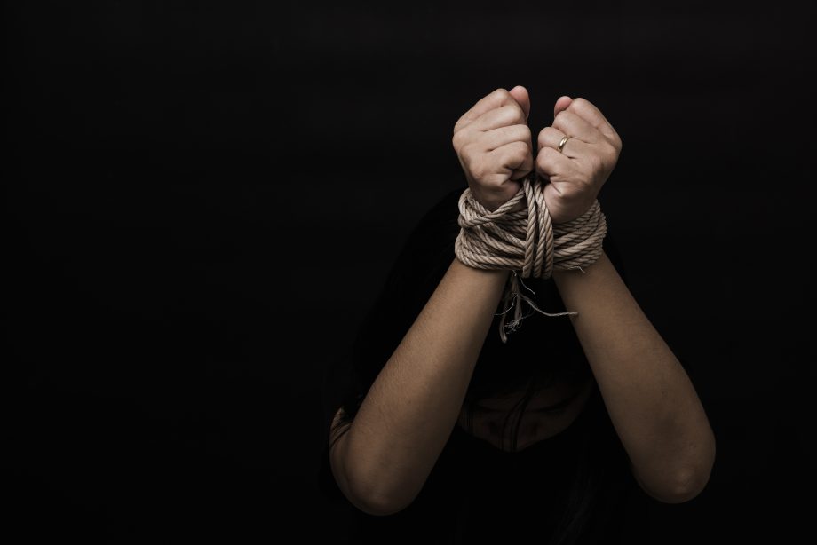 Eine Person, deren Hände mit einem Seil gefesselt sind, hebt vor einem dunklen Hintergrund die Fäuste und erinnert so an die Notlage eines Bitcoin-Entführers, der in Haft sitzt.