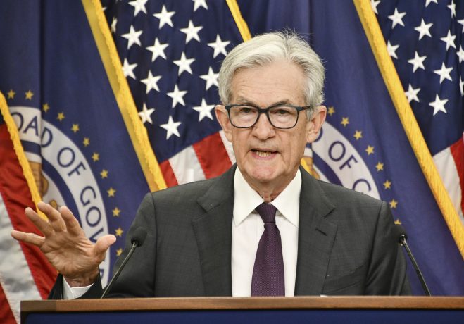 Jerome Powell spricht über Zinsen, Bitcoin und die Aktienmärkte, im Hintergrund ist die USA-Flagge.