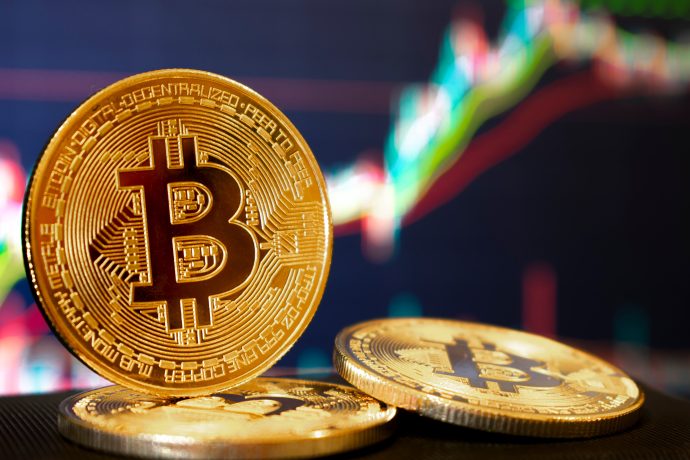 Nahaufnahme von drei physischen Bitcoin-Token mit einem digitalen Preisdiagramm, das im unscharfen Hintergrund einen Aufwärtstrend zeigt und das wachsende Interesse an Bitcoin-Investitionen unterstreicht.