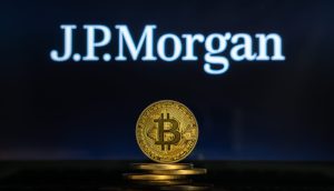 Eine goldene Bitcoin-Münze steht im Mittelpunkt und hebt die digitale Währung vor einem verschwommenen J.P. Morgan-Logo auf dunklem Hintergrund hervor.