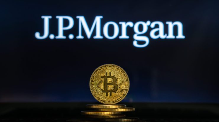 Eine goldene Bitcoin-Münze steht im Mittelpunkt und hebt die digitale Währung vor einem verschwommenen J.P. Morgan-Logo auf dunklem Hintergrund hervor.