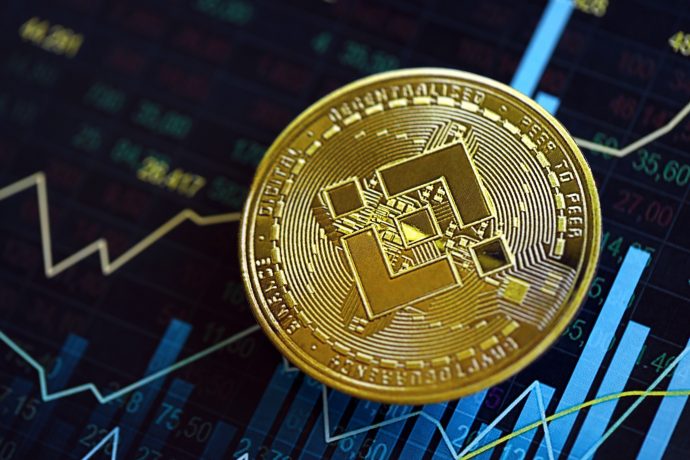 Eine goldene BNB Binance-Münze ruht auf einem digitalen Bildschirm, der ein buntes Kryptowährungspreisdiagramm mit schwankenden Linien und Zahlen anzeigt.