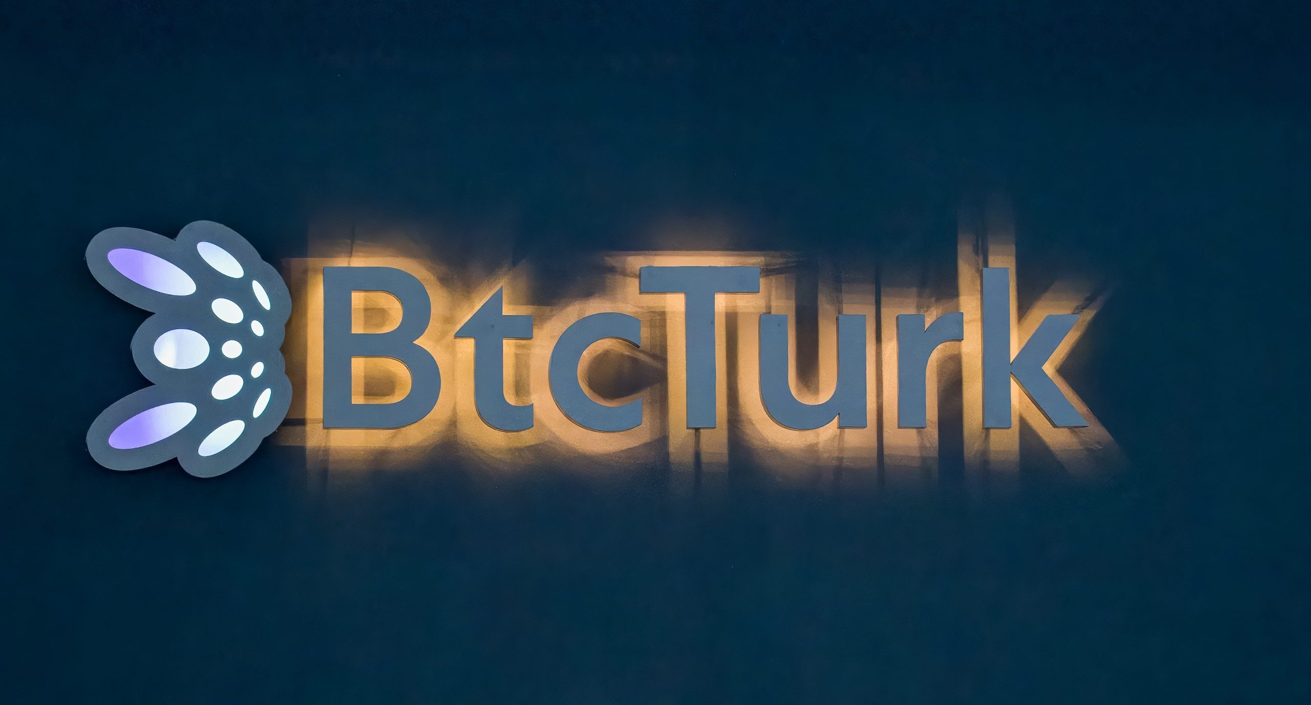 Das Bild zeigt ein beleuchtetes BtcTurk-Logo und -Zeichen auf dunklem Hintergrund, das die Krypto-Börse darstellt.