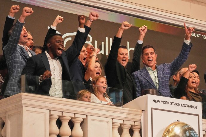 Eine Gruppe von Menschen feiert auf dem Balkon der New Yorker Börse und jubelt mit erhobenen Fäusten während eines IPO-Debüt-Glockenläutens.