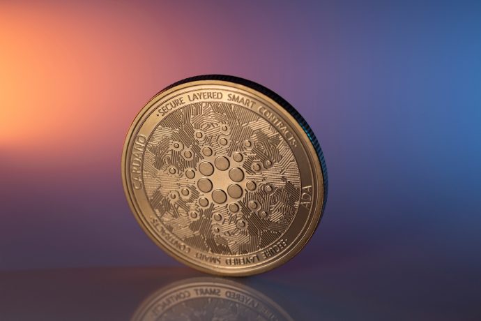 Eine Cardano (ADA) Kryptowährungsmünze steht aufrecht vor einem Hintergrund mit Blau- und Orangetönen, der die Innovation hinter Cardano hervorhebt.