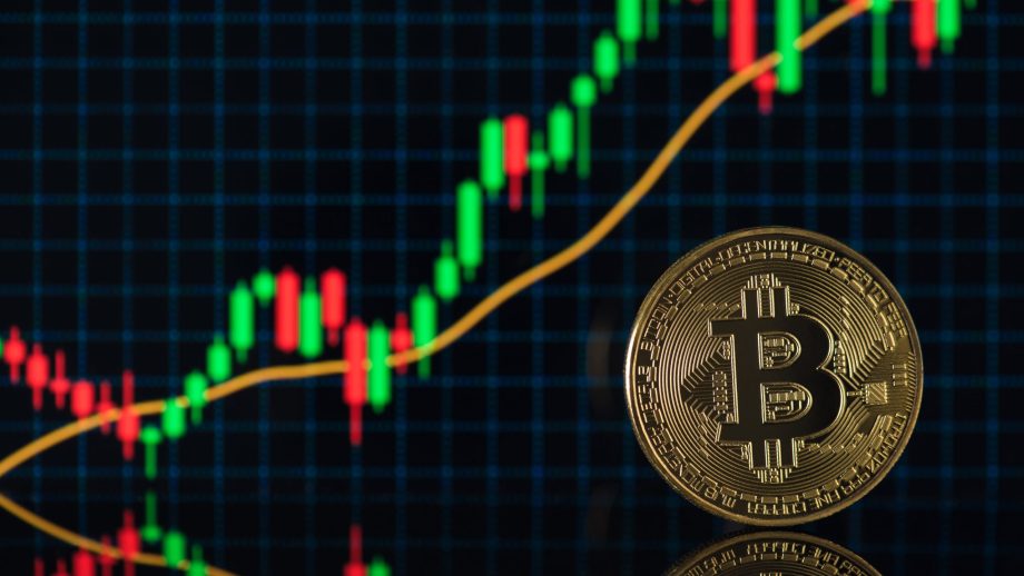 Eine goldene Bitcoin-Münze steht vor einem digitalen Bildschirm, der einen Candlestick-Chart mit steigenden grünen und roten Kurstrends anzeigt, der den aktuellen BTC-Kurs widerspiegelt und die neueste Bitcoin-Prognose eines Experten unterstützt.
