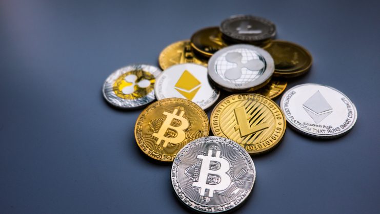 Ein verstreuter Haufen physischer Krypto-Münzen mit Kryptowährungslogos, darunter Bitcoin, Ethereum, Ripple und Litecoin, liegt auf einer grauen Fläche.