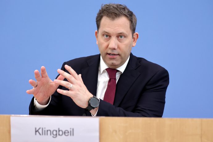 Ein Mann in Anzug und Krawatte spricht an einem Podium mit einem Namensschild, auf dem Klingbeil steht, und gestikuliert mit seinen Händen während einer Pressekonferenz mit automatisch gespeichertem Entwurf.