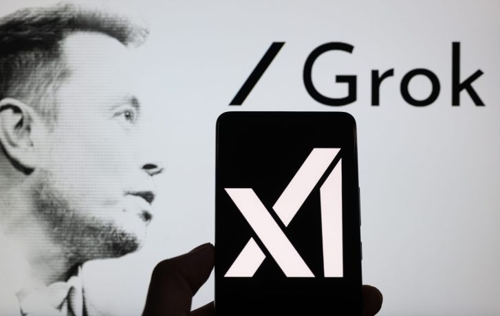 Ein Smartphone zeigt das xAI-Logo vor einem Bildschirm mit einem Graustufen-Profilfoto, dem Wort Grok und einem subtilen Hinweis auf Bitcoin.