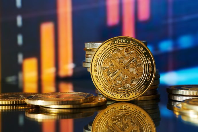 Stapel von XRP-Münzen werden vor einem unscharfen Finanzchart mit orangen und blauen Balken im Hintergrund angezeigt.