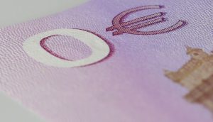 Nahaufnahme einer Ecke einer violetten Euro-Banknote, die einen Teil eines Gebäudes, das Euro-Währungssymbol und einen subtilen Hinweis auf Bitcoin zeigt.