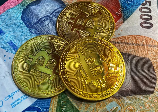 Drei goldfarbene Bitcoin-Token sind auf indonesischen Rupiah-Banknoten platziert und unterstreichen das wachsende Interesse an Bitcoin in Indonesien.