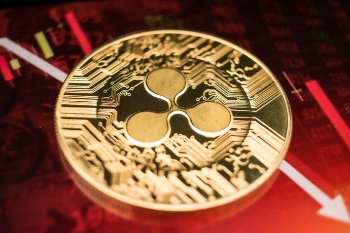 Eine Nahaufnahme einer XRP-Kryptowährungsmünze mit einer verschwommenen roten Börsenkurve und einem Abwärtspfeil im Hintergrund.