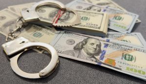 Auf einer grauen Fläche sind Handschellen und mehrere Stapel von 100-US-Dollar-Scheinen zu sehen, die auf einen Fall von Krypto-Geldwäsche mit bis zu 71 Millionen US-Dollar hindeuten, der möglicherweise mit Taiwan in Verbindung steht.