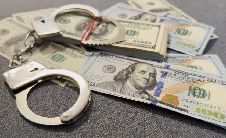 Auf einer grauen Fläche sind Handschellen und mehrere Stapel von 100-US-Dollar-Scheinen zu sehen, die auf einen Fall von Krypto-Geldwäsche mit bis zu 71 Millionen US-Dollar hindeuten, der möglicherweise mit Taiwan in Verbindung steht.