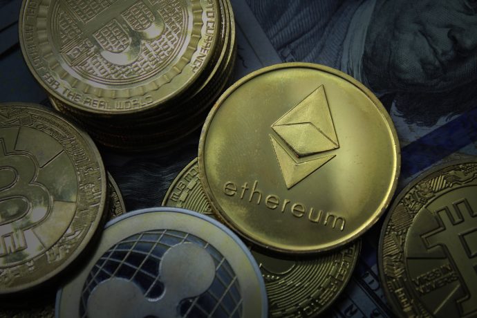 Nahaufnahme mehrerer Krypto-Münzen, mit einer prominenten Ethereum-Münze in der Mitte, während im Hintergrund Bitcoin- und Ripple-Münzen zu sehen sind.
