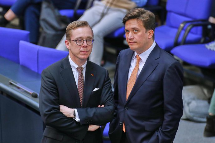 Zwei Männer in dunklen Anzügen stehen im Plenarsaal des Deutschen Bundestages und unterhalten sich. Beide wirken konzentriert und ernst, im Hintergrund sind die typischen blauen Sitze des Parlaments zu sehen. Das Bild vermittelt den Eindruck eines politischen Gesprächs auf hoher Ebene – passend zum aktuellen Diskurs über den Krypto-Masterplan der CDU, der Themen wie Bitcoin, Blockchain und Steuerpolitik umfasst.
