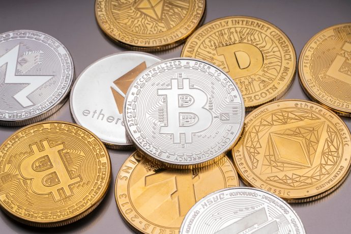 Verschiedene physische Krypto-Münzen, die verschiedene Kryptowährungen repräsentieren, darunter Bitcoin, Ethereum, Litecoin, Monero und Dogecoin, sind auf einer flachen Oberfläche verstreut.