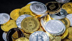Ein Stapel verschiedener physischer Münzen, darunter Bitcoin, Ethereum und Litecoin, die verschiedene Kryptowährungen auf einem schwarzen Hintergrund repräsentieren.