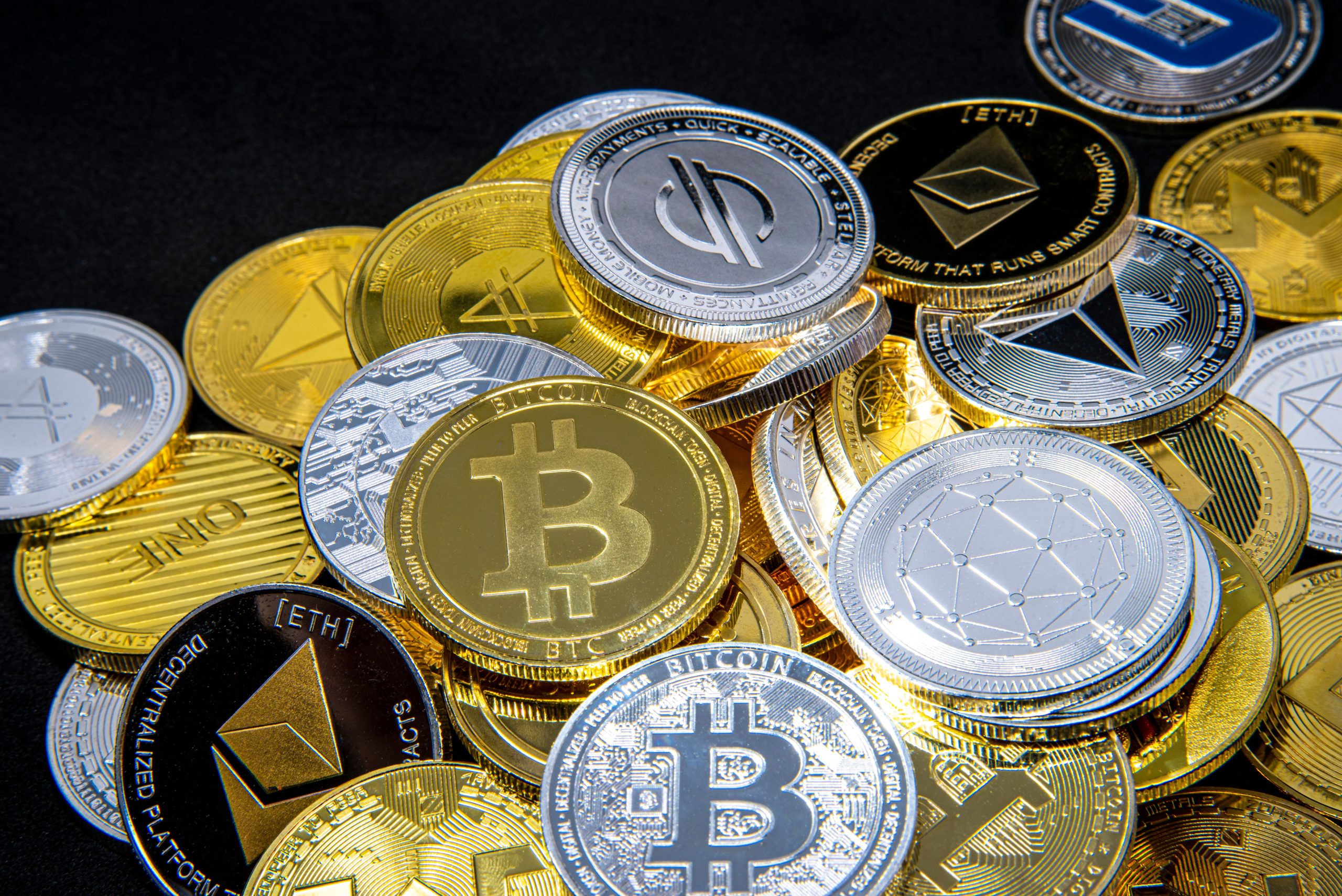 Ein Stapel verschiedener physischer Münzen, darunter Bitcoin, Ethereum und Litecoin, die verschiedene Kryptowährungen auf einem schwarzen Hintergrund repräsentieren.