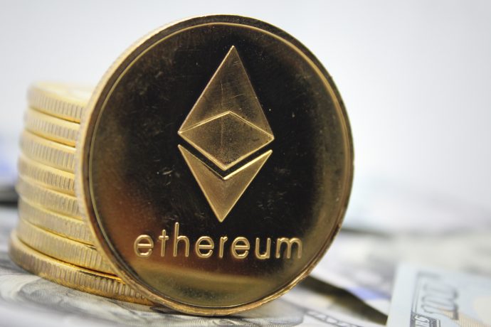 Ein Stapel goldfarbener Ethereum-Münzen, in die das Ethereum-Logo und das Wort "Ethereum" eingraviert sind, ruht auf US-Dollarnoten.