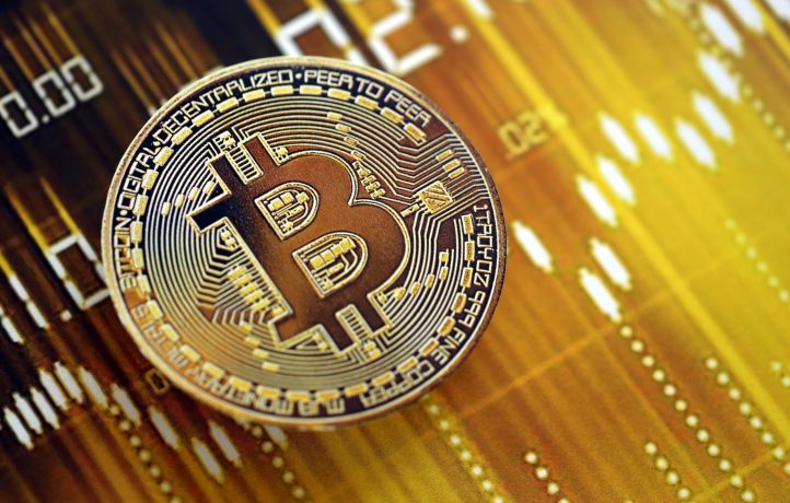 Eine physische Darstellung einer Bitcoin-Münze wird vor einem digitalen Hintergrund mit gelben und goldenen Diagrammlinien gezeigt, die die Unwägbarkeiten eines Bärenmarktes widerspiegeln.