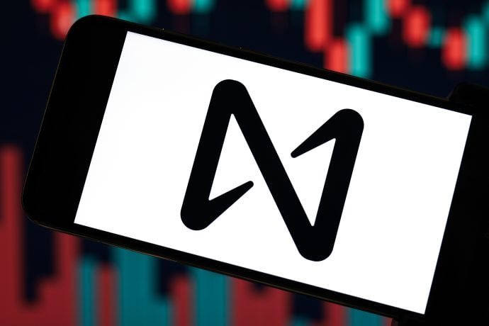 Ein Smartphone zeigt das Logo des NEAR-Protokolls auf seinem Bildschirm an, mit einem verschwommenen Finanzdiagramm aus roten und blauen Balken im Hintergrund, das die Rolle der KI-Technologien im modernen Blockchain-Finanzwesen hervorhebt.