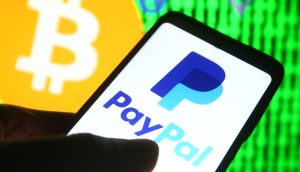 Ein Smartphone zeigt im Vordergrund das PayPal-Zahlungs-Logo, dahinter ist ein großes Bitcoin-Symbol und ein verpixelter grüner Hintergrund zu sehen.