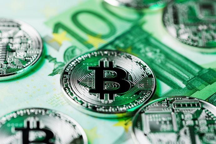 Silberne Bitcoin-Münzen auf grünen 100-Euro-Banknoten, die das Konzept von Krypto und traditionellem Geld veranschaulichen.