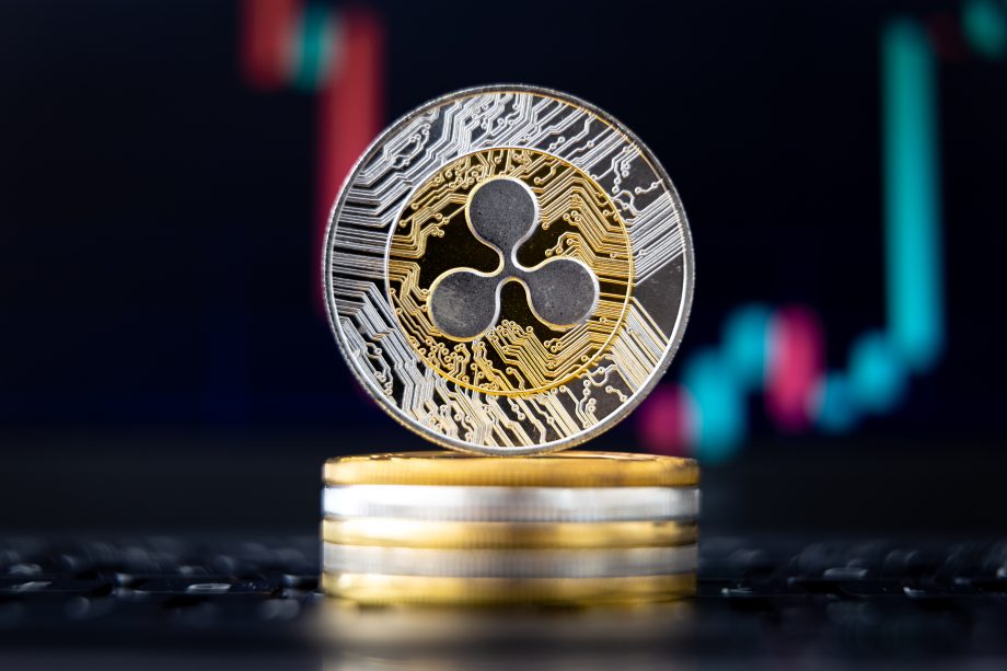 Eine Nahaufnahme einer XRP-Kryptowährungsmünze, die auf einem Stapel von Münzen steht, mit einem unscharfen Finanzdiagramm im Hintergrund.