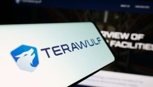 Ein Smartphone-Bildschirm zeigt das TeraWulf-Logo und den Namen, im Hintergrund ist eine unscharfe TeraWulf-Website mit Bitcoin-Thema zu sehen.