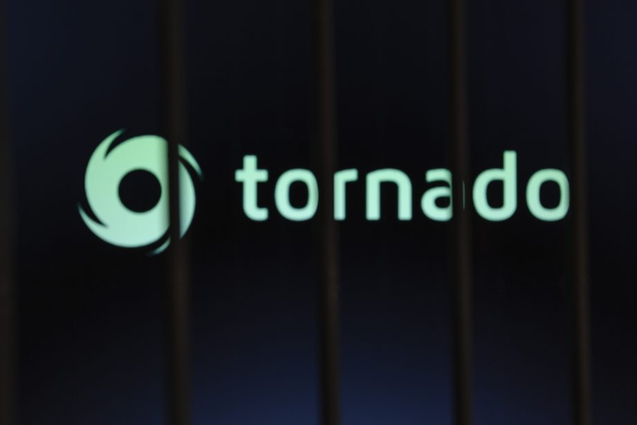 Ein unscharfes Bild mit dem Schriftzug Tornado Cash und einem wirbelnden Logo, das teilweise von dunklen vertikalen Balken im Vordergrund verdeckt wird.