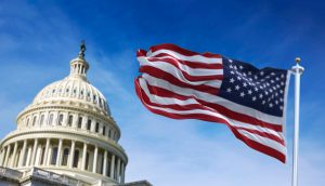 Im Hintergrund steht das US-Kapitol, im Vordergrund weht die amerikanische Flagge vor blauem Himmel - eine Erinnerung an Grundprinzipien wie die des Howey-Tests im amerikanischen Wertpapierrecht.