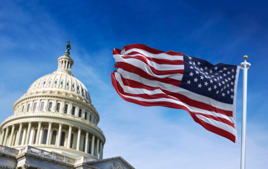 Im Hintergrund steht das US-Kapitol, im Vordergrund weht die amerikanische Flagge vor blauem Himmel - eine Erinnerung an Grundprinzipien wie die des Howey-Tests im amerikanischen Wertpapierrecht.
