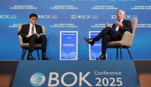 Zwei Männer sitzen auf der BOK Conference 2025 auf einer Bühne, zwischen ihnen ist das Event-Branding und eine Anzeige mit der Aufschrift Chang Yong Rhee zu sehen, und diskutieren über DeFi und die Auswirkungen auf die traditionellen Rollen von Bankern.