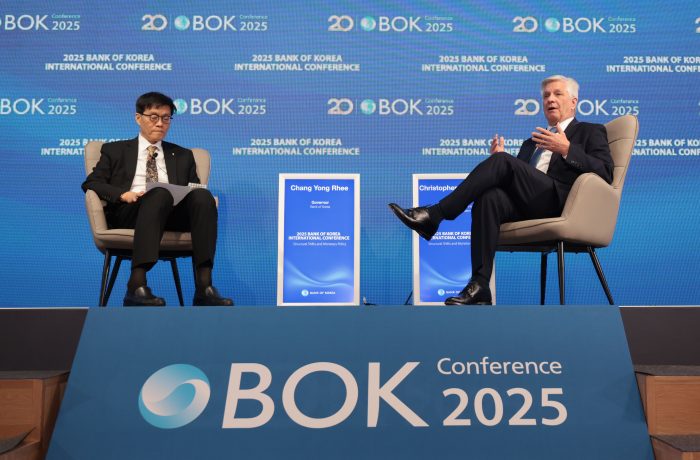 Zwei Männer sitzen auf der BOK Conference 2025 auf einer Bühne, zwischen ihnen ist das Event-Branding und eine Anzeige mit der Aufschrift Chang Yong Rhee zu sehen, und diskutieren über DeFi und die Auswirkungen auf die traditionellen Rollen von Bankern.